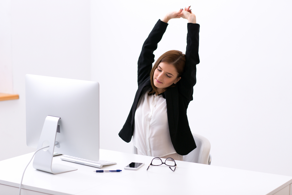 Businesswoman sitting at the table in office and stretching her hands above her head