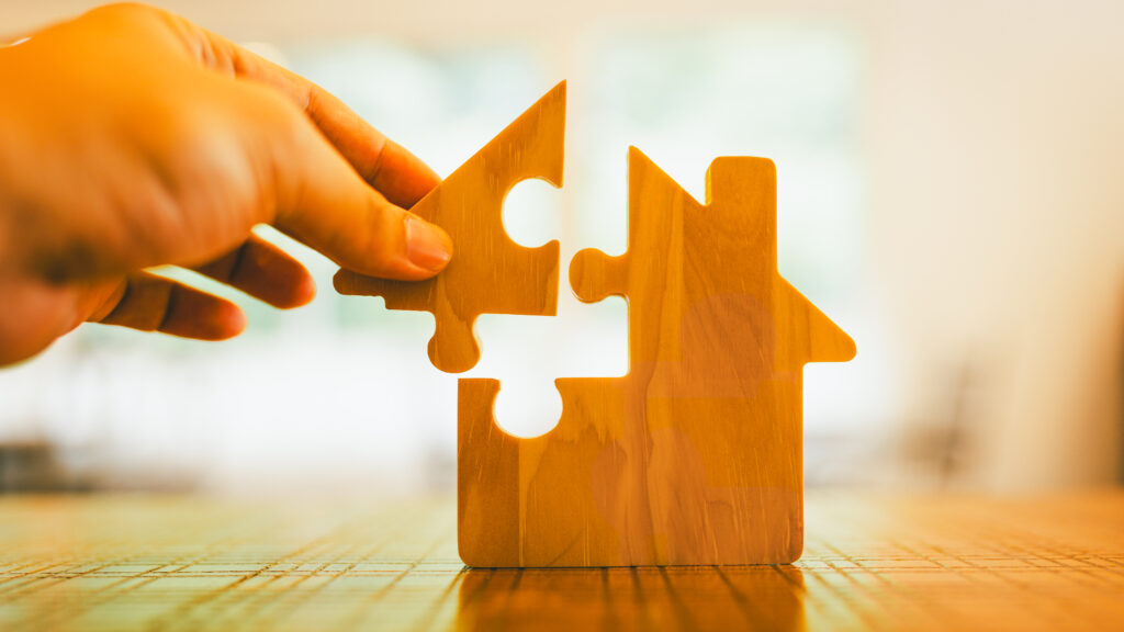 Hand holding a wooden piece of a puzzle in the shape of a house.